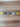 A pet collar with a blue and pink patterned fabric strap and bright yellow plastic hardware, laid flat on a light brown wood floor.